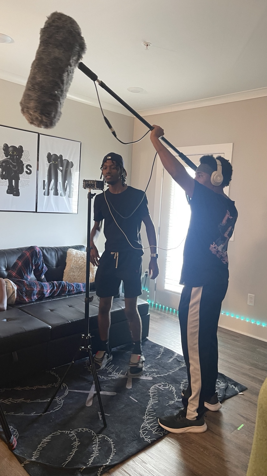 A camera and lighting crew prepare to film a performer in a living room.