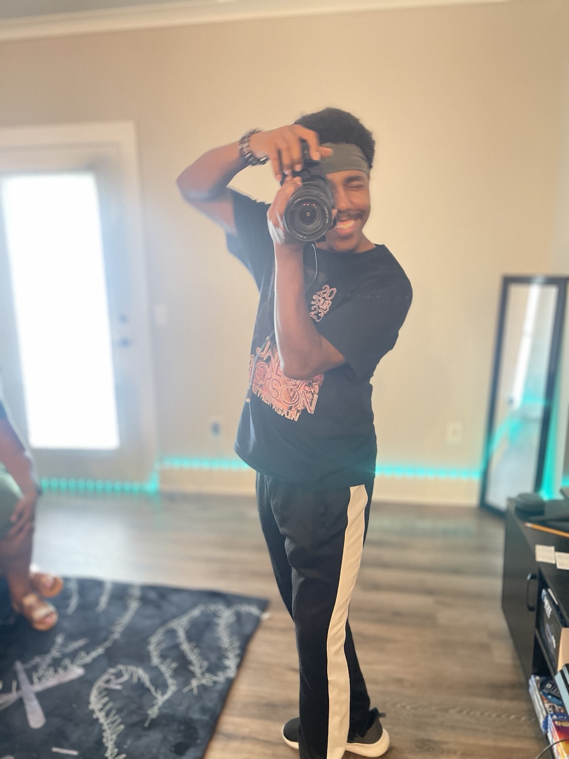 A filmmaker smiles while holding a camera on set.