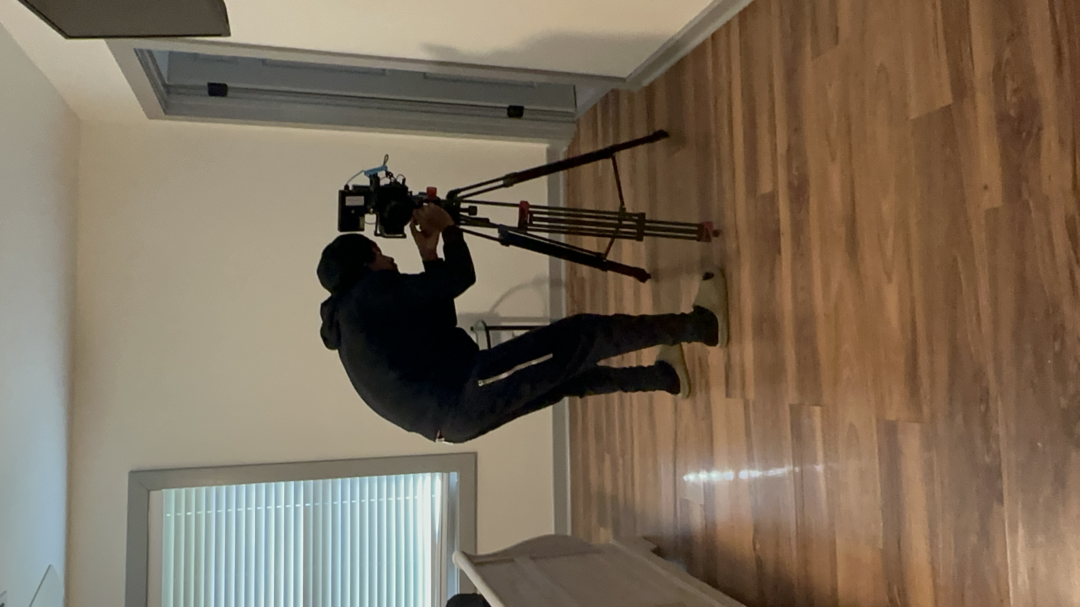 Camera operator adjusts a tripod in a bedroom set.