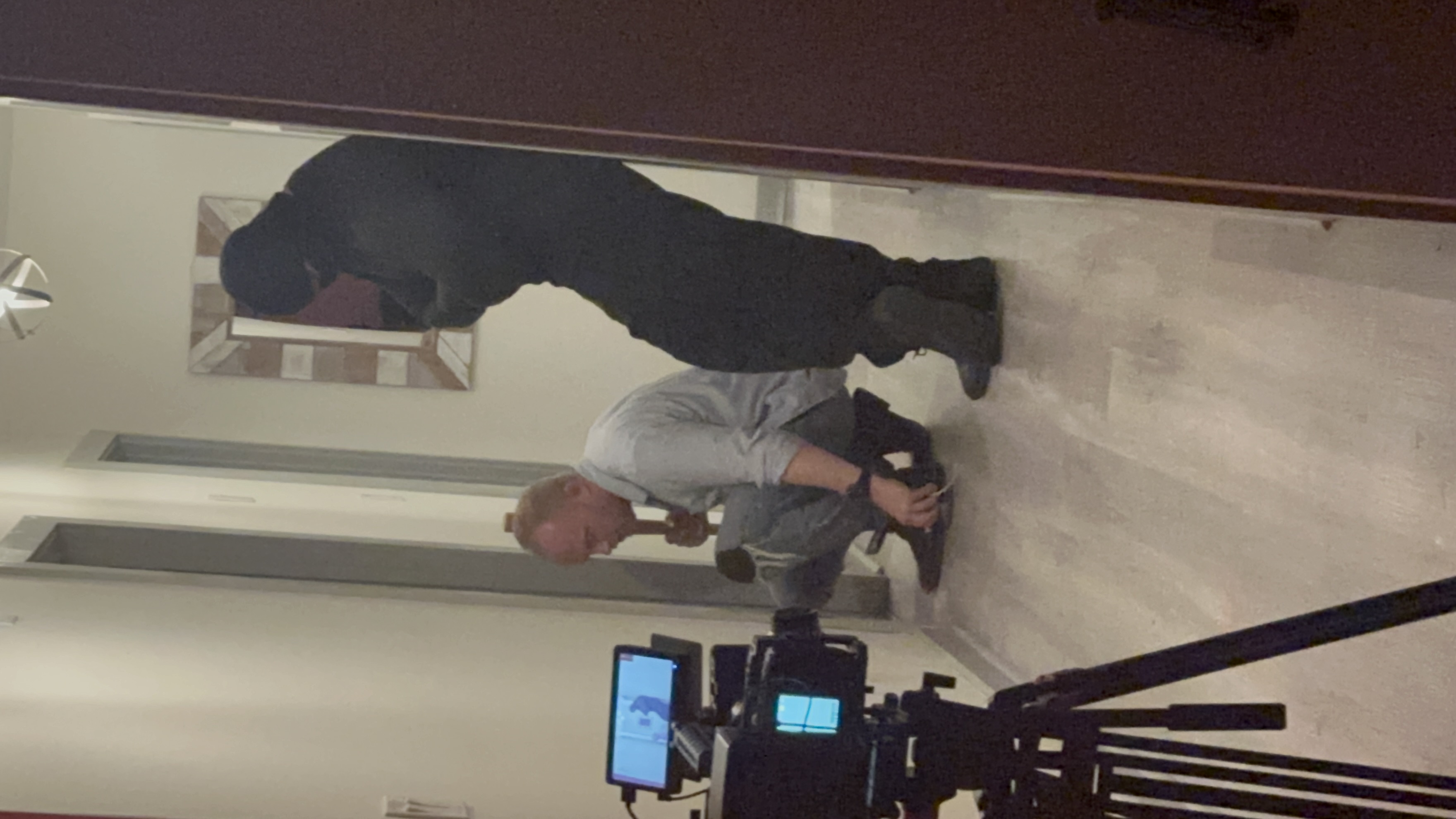 A camera frames two performers in a narrow hallway.