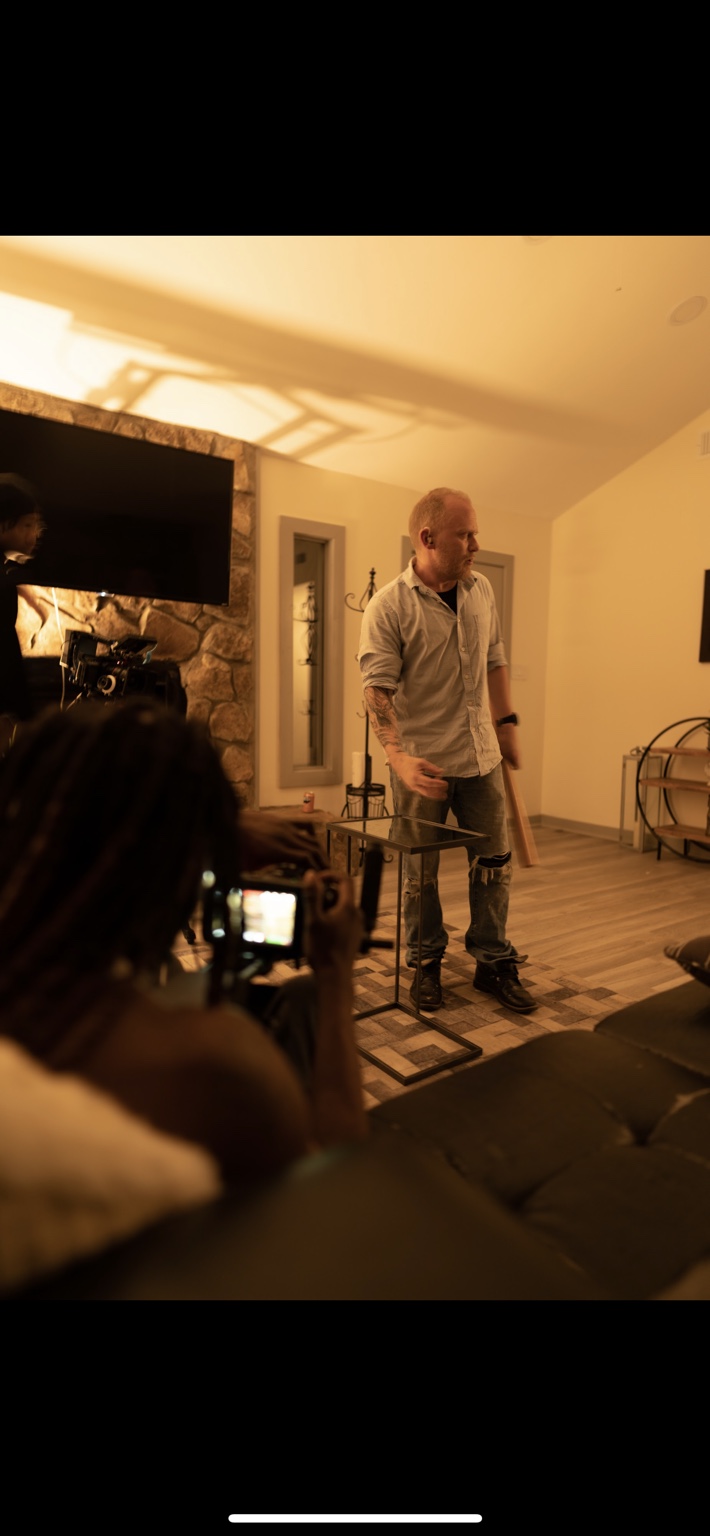 A camera operator films a performer in a warmly lit living room.