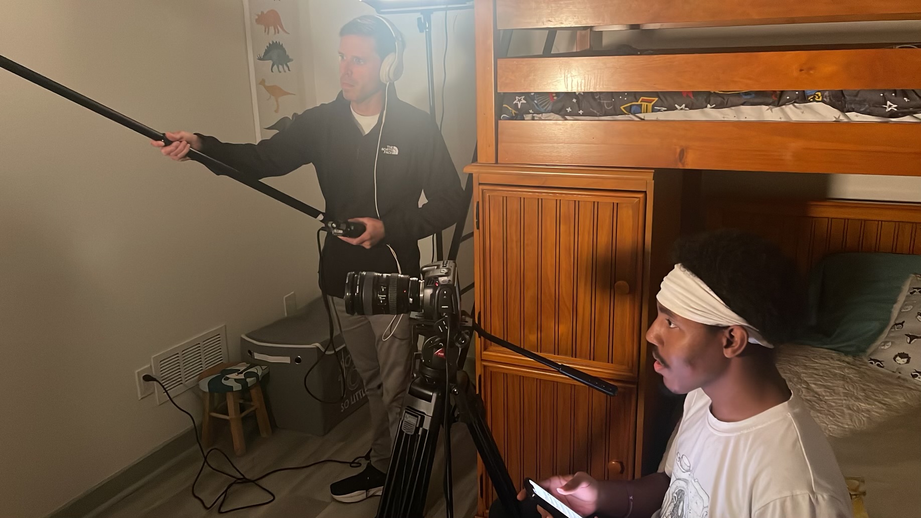 A sound operator holds a boom microphone beside a bedroom set.