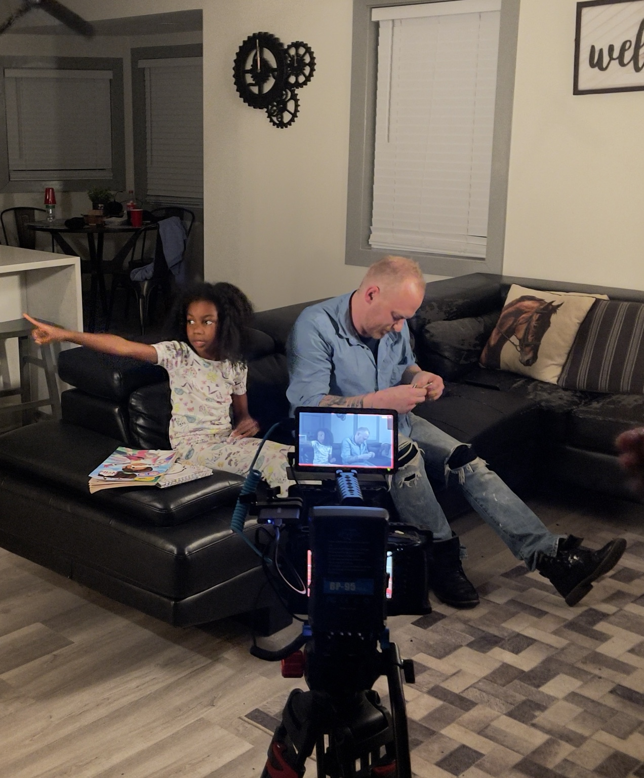 Cast and crew prepare a scene around a camera and lighting equipment.
