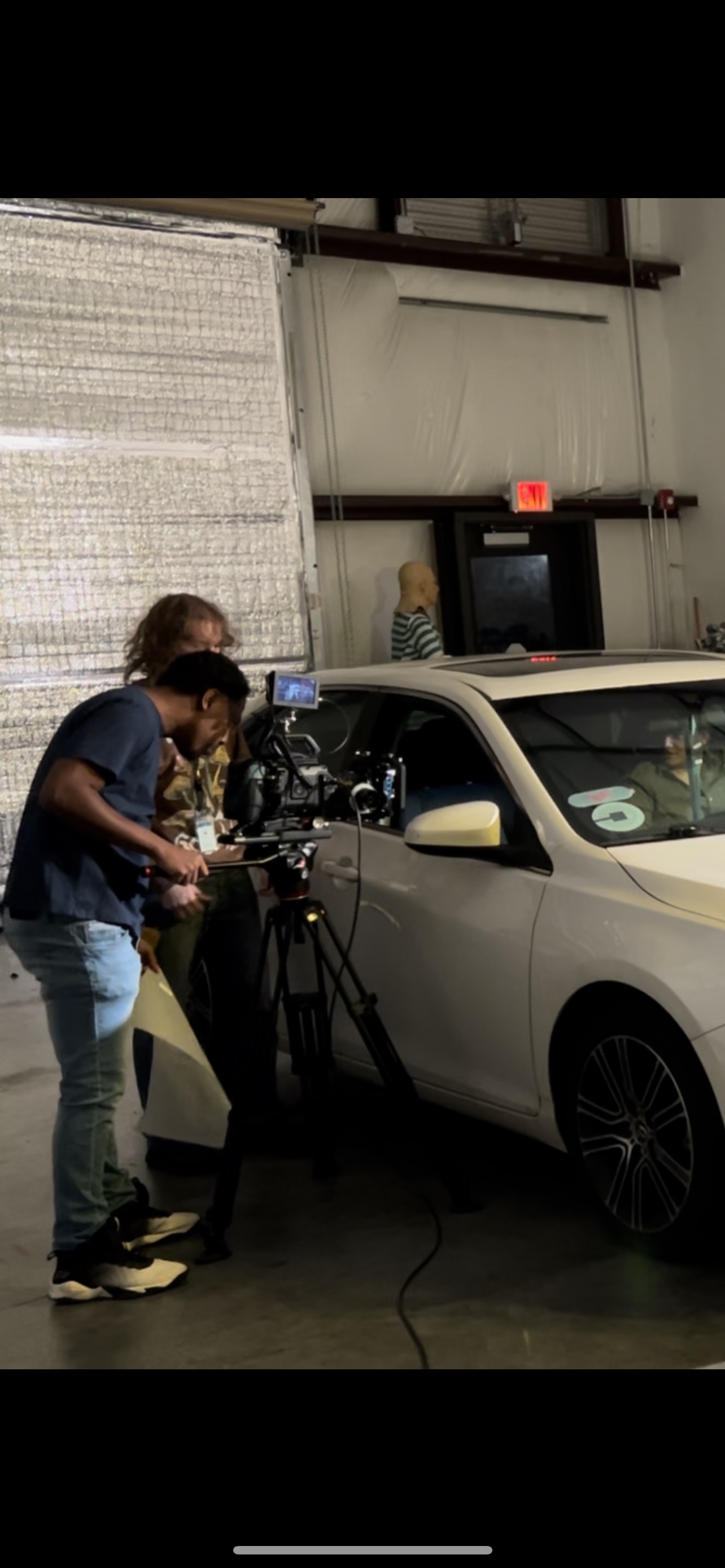 Camera crew films beside a white car on an indoor set.